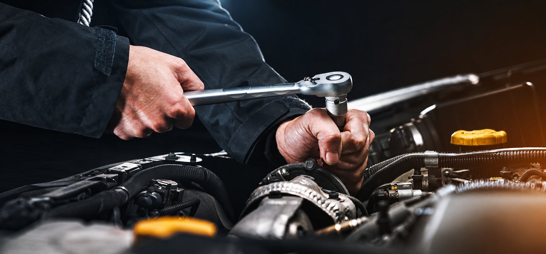 Les mains d'un mécanicien utilisent une clé à cliquet pour travailler sur un moteur de voiture sous le capot ouvert.