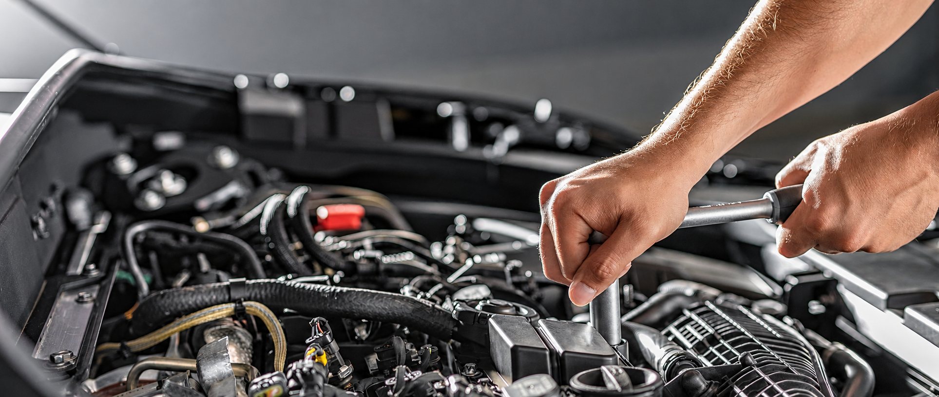 Les mains d'un mécanicien actionnent une clé à cliquet sur un moteur de voiture dont le capot est ouvert.